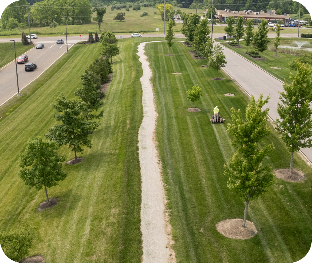 Drone view of expansive commercial property with professionally maintained striped lawn patterns, mature trees, and landscaping demonstrating comprehensive grounds care