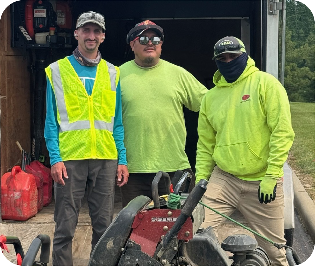 Three H&M Landscaping crew members in high-visibility safety gear standing together with landscaping equipment at job site, representing professional commercial landscaping services