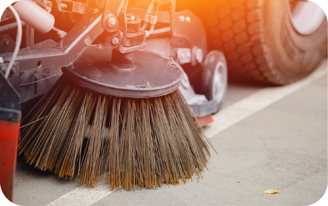 parking-lot-sweeper-brush-closeup Close-up view of industrial parking lot sweeper brush in action, demonstrating professional street sweeping equipment for commercial property maintenance